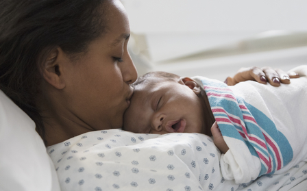 A woman lying on the bed and kissing her baby on the forehead
