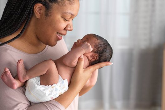 A smiling mother holds her diapered newborn
