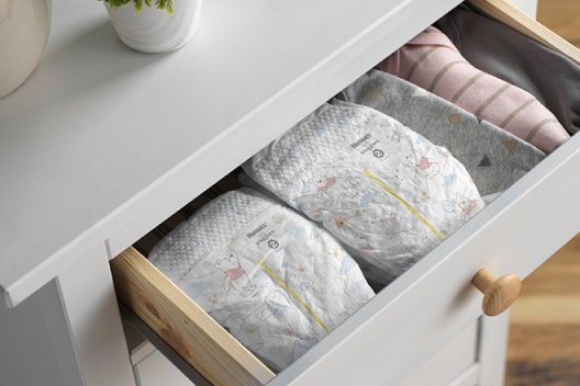The top drawer of a white dresser is pulled out to display multiple Huggies Little Snugglers Diapers with wetness indicators