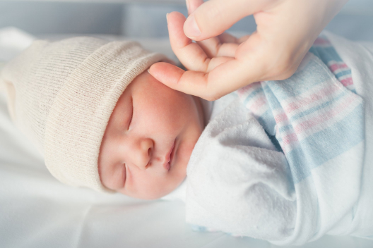 A parent softly touching a sleeping baby's cheeks with their fingers