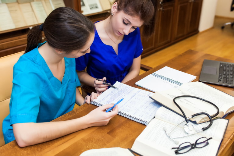 Two Healthcare nurses sitting and studying with some open books kept on the table