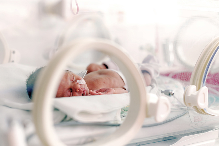 NICU baby in isolette with feeding tube