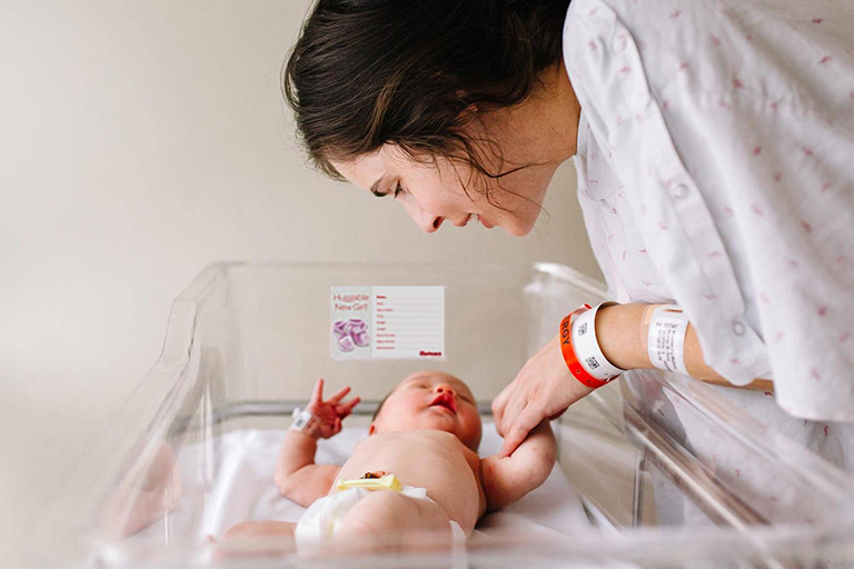 A mother looking at her newborn baby lying in an open hospital baby container 